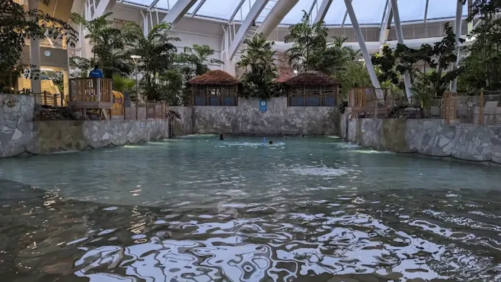 Quiet wave pool at Center Parcs Woburn Forest with tropical greenery, lifeguard station, and thatched cabanas beneath a glass dome ceiling.