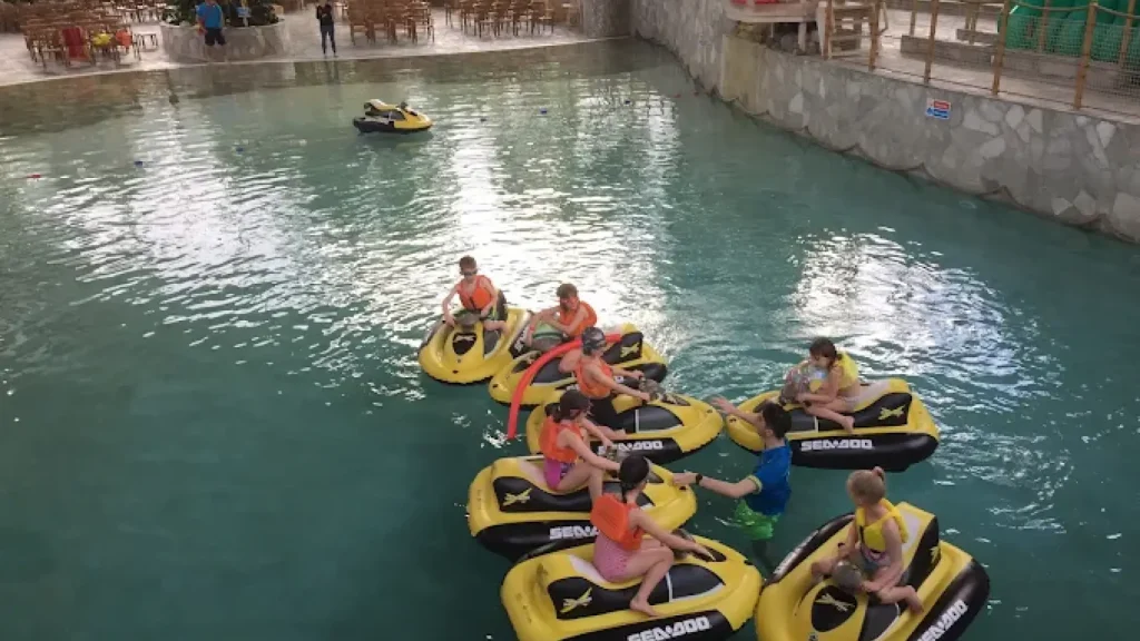 Kids enjoying a mini jet ski activity at Center Parcs Woburn Forest indoor pool, guided by an instructor and wearing safety vests.