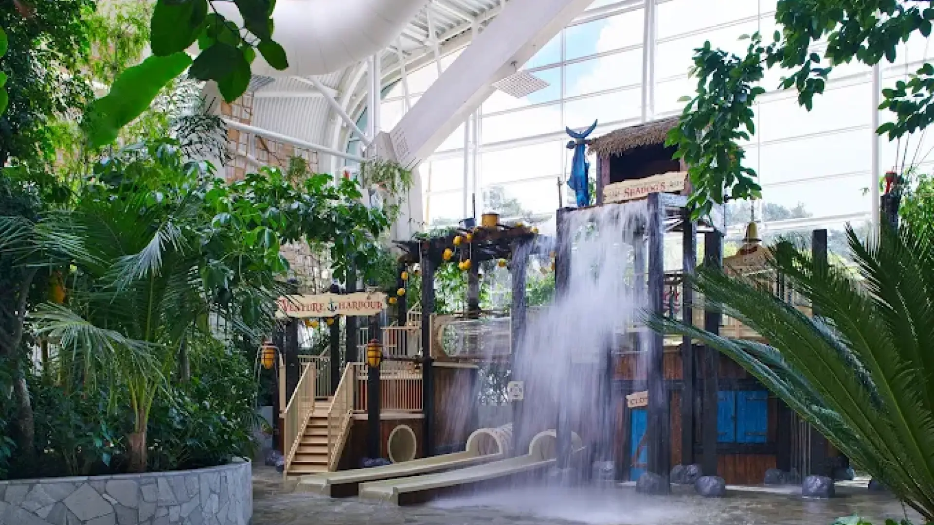 Venture Harbour kids’ water play area at Center Parcs Woburn Forest with slides, splash features, and a large tipping bucket in a tropical indoor setting.