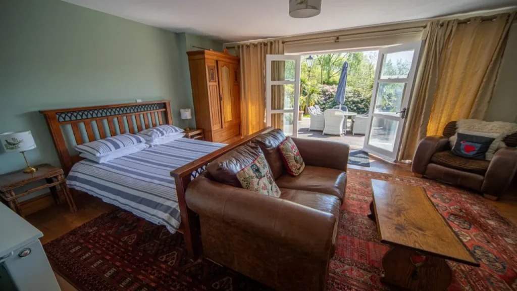 Cosy guest room with double bed, leather sofa, and garden patio access at Chained Oak Farm B&B near Alton Towers.