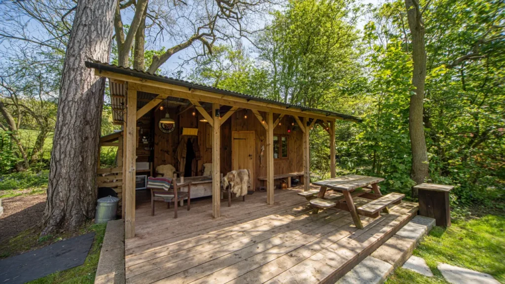 Wooden cabin with outdoor seating and picnic table surrounded by forest at Chained Oak Farm B&B near Alton Towers.