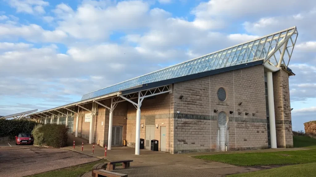 Exterior view of Dunbar Swimming Pool in East Lothian, Scotland, showing modern architecture with a slanted glass roof under a blue sky.