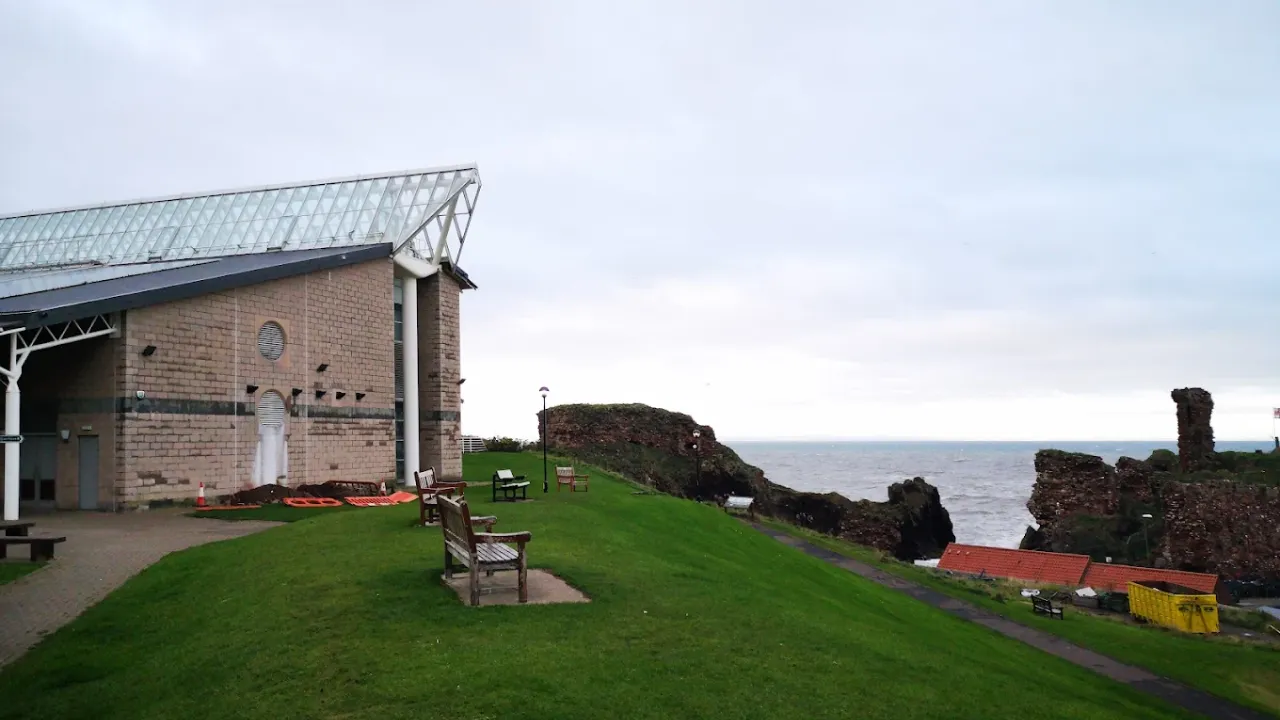 Side view of Dunbar Swimming Pool overlooking grassy cliffs, Dunbar Castle ruins, and the North Sea on a cloudy day in East Lothian.