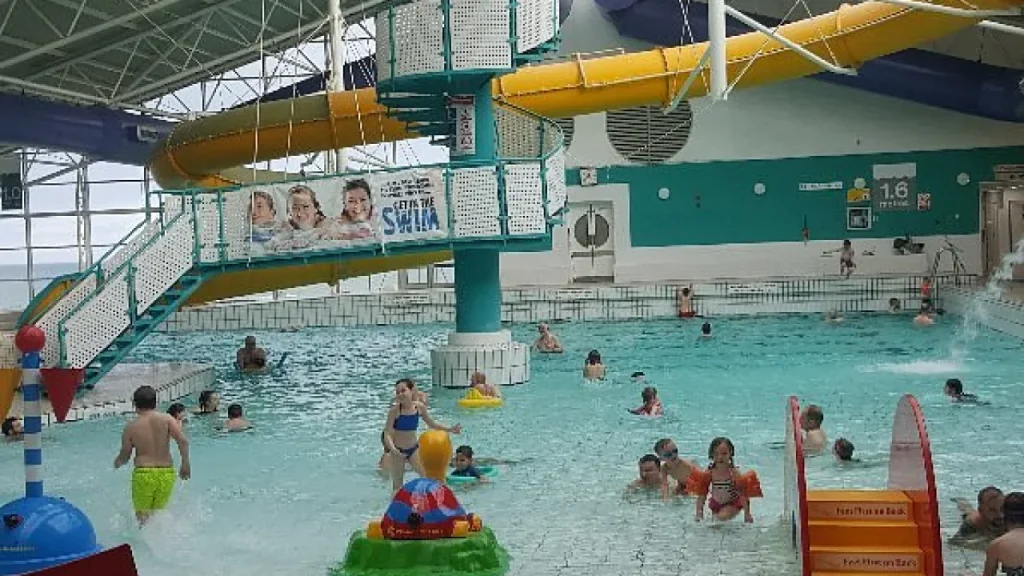Children and families playing in the shallow area of Dunbar Swimming Pool with colourful water toys and a yellow indoor flume slide.