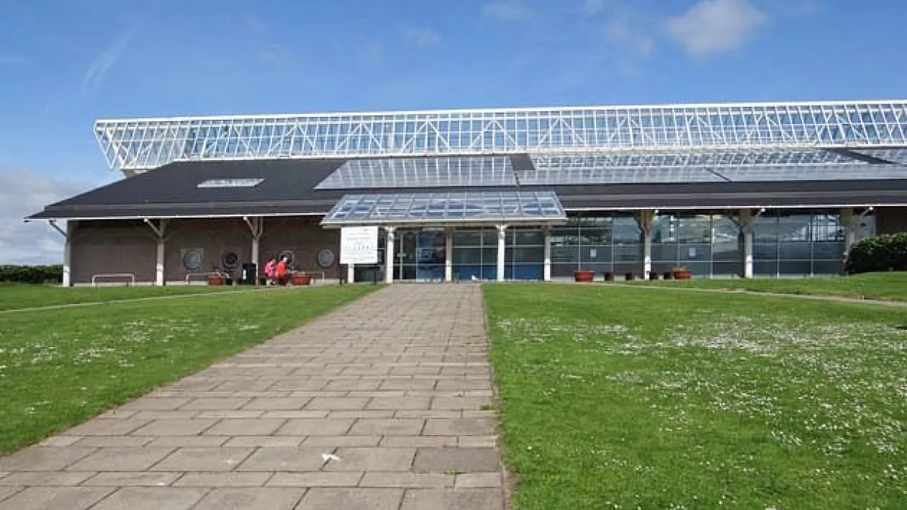 Exterior of Dunbar Swimming Pool with glass roof, entrance path, and grassy lawn on a bright, clear day in East Lothian.