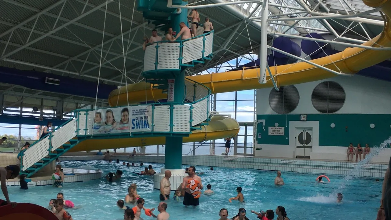 Busy scene at Dunbar Swimming Pool with people lined up for the yellow flume, and families swimming and playing in the large indoor pool.