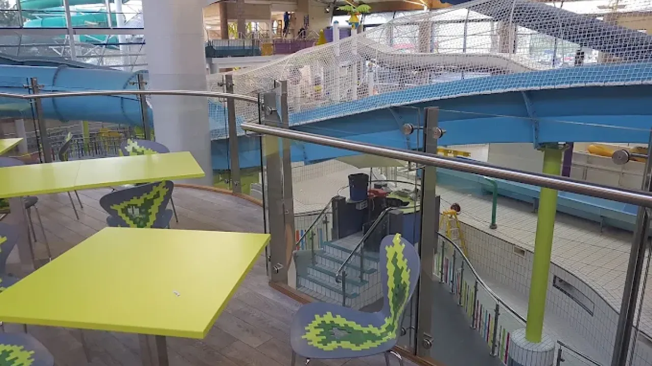Indoor seating area with lime green tables and modern chairs overlooking water slides and the pool at Lagan Valley LeisurePlex in Lisburn.