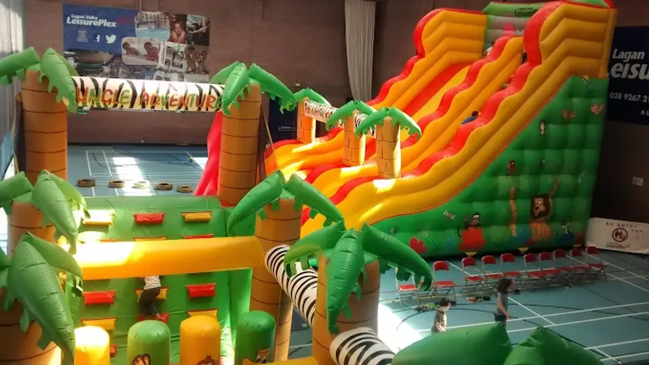 Indoor inflatable play area at Lagan Valley LeisurePlex featuring palm tree designs, climbing walls, and a large red and yellow jungle-themed slide.
