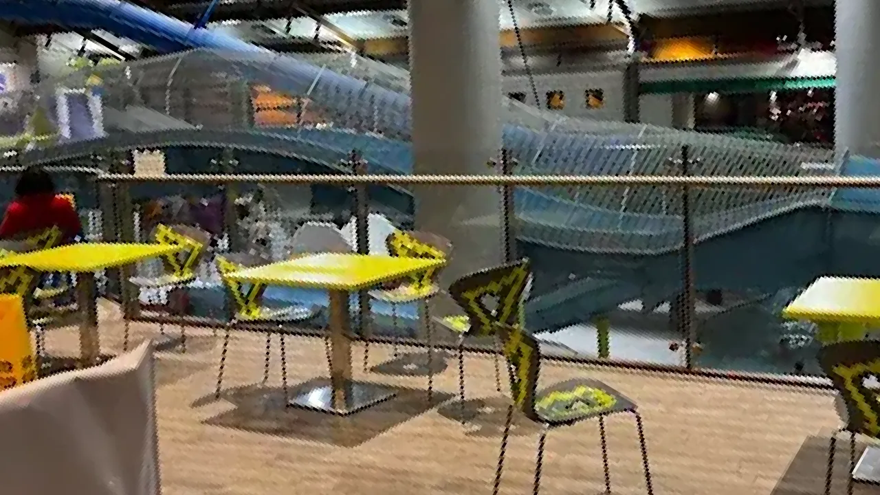 Indoor café area with lime green tables and abstract-pattern chairs overlooking enclosed water slides at Lagan Valley LeisurePlex in Lisburn.
