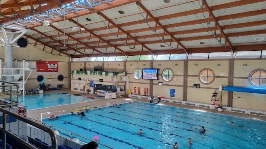 Indoor view of the 25-metre lane swimming pool and adjacent diving pool at Lagan Valley LeisurePlex with swimmers and instructors in action.