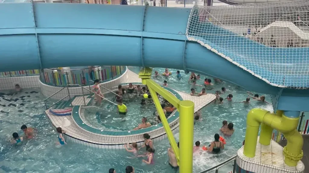 Busy indoor leisure pool at Lagan Valley LeisurePlex filled with children and adults swimming beneath a large blue water slide.