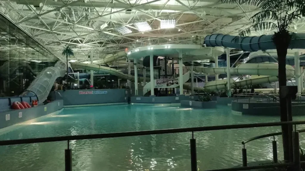 Illuminated indoor wave pool and multiple water slides at The LC Swansea during the evening, with reflections on calm water and themed decor.