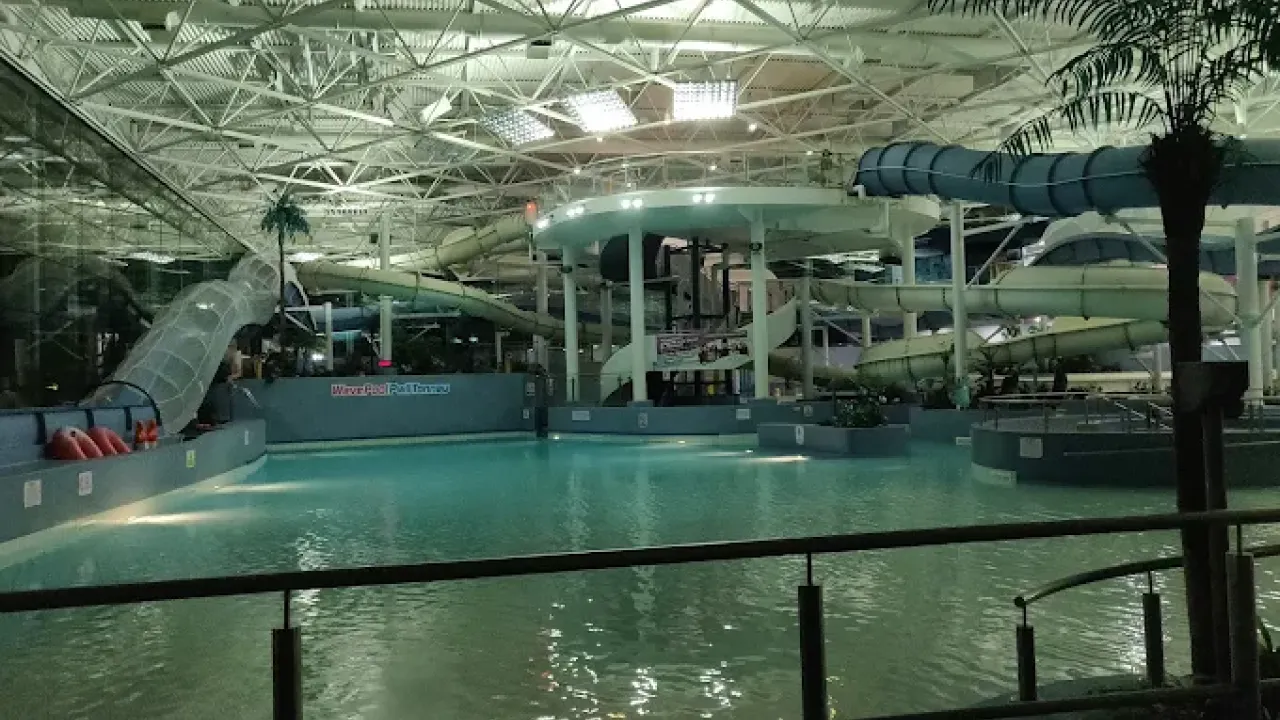 Illuminated indoor wave pool and multiple water slides at The LC Swansea during the evening, with reflections on calm water and themed decor.