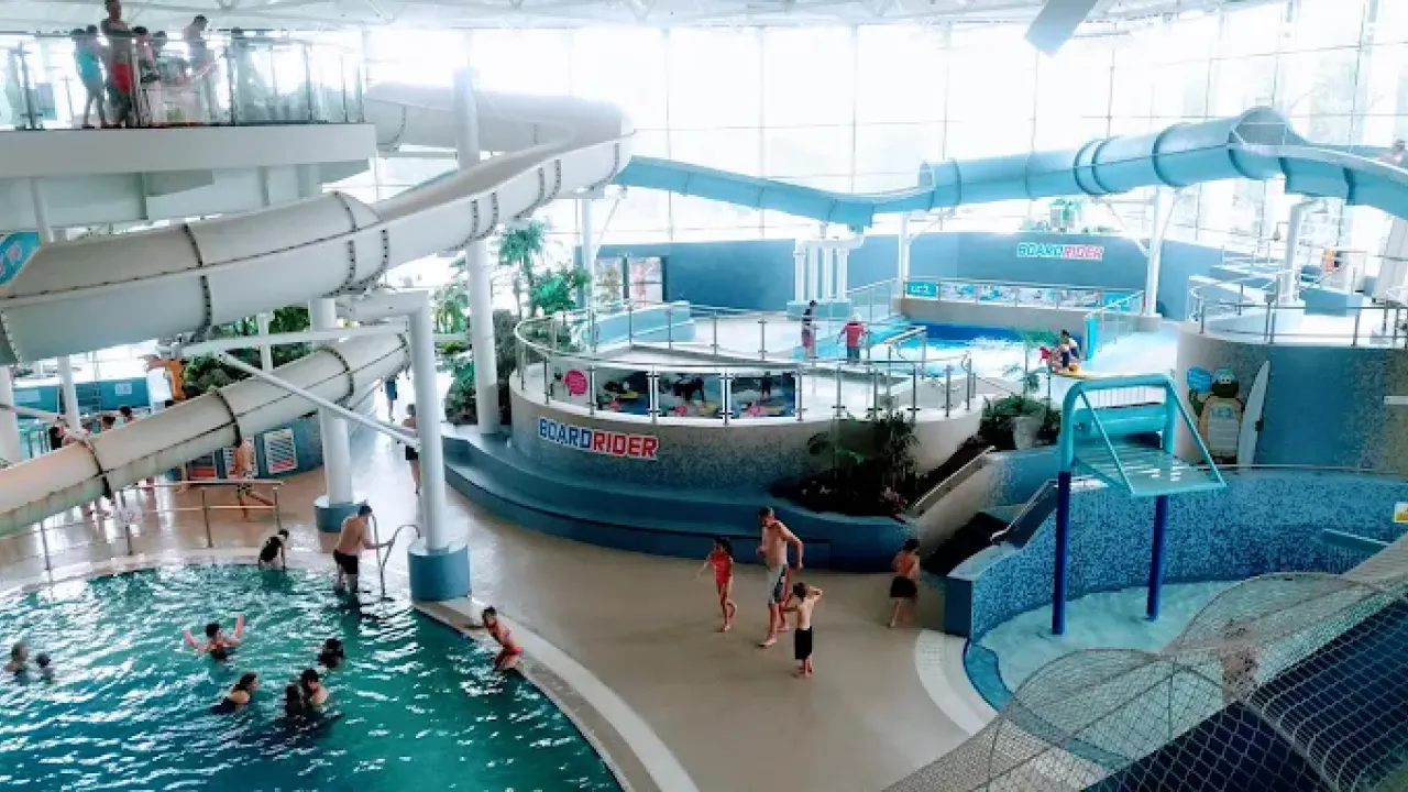 The LC Swansea waterpark with winding water slides, the Boardrider surf simulator, splash zones, and families enjoying indoor swimming areas.