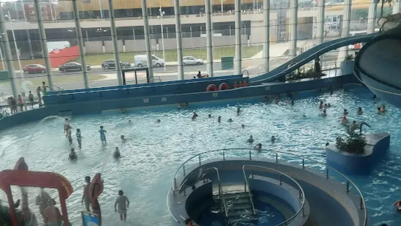 Crowds enjoying the indoor wave pool at The LC Swansea, with a waterslide entry, spray features, and wide windows offering natural light.