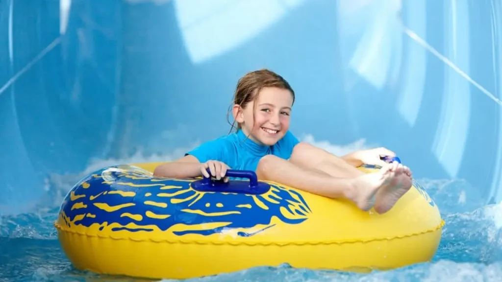 Smiling child riding an inflatable yellow tube down a water slide at The LC Swansea, enjoying a fun and safe indoor waterpark experience.