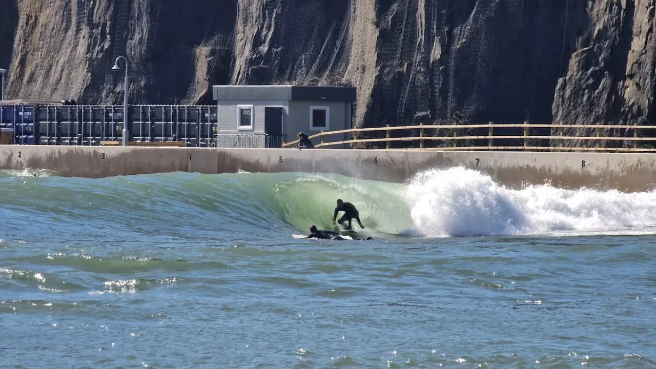 Surfer catching a barrel wave at Lost Shore Surf Resort Edinburgh with rocky cliff walls and engineered surf lagoon infrastructure in the background.