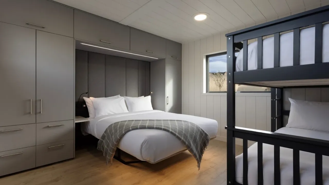 Interior of a family lodge at Lost Shore Surf Resort Edinburgh featuring a double bed, bunk beds, built-in wardrobes, and natural lighting.