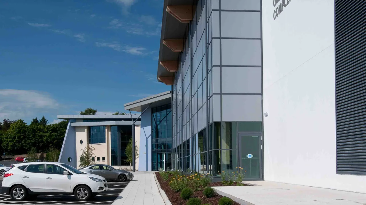 Omagh Leisure Complex exterior showing glass entrance, modern design, and car park on a bright sunny day.