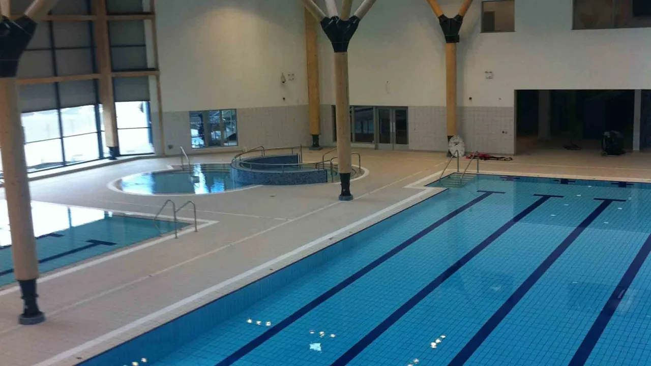 Indoor pool area at Omagh Leisure Complex featuring lane pool, teaching pool, and circular spa pool in a bright, tiled space.