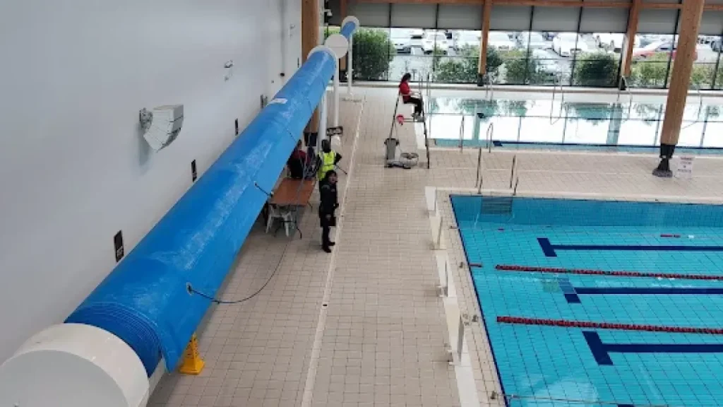 Lifeguards at Omagh Leisure Complex poolside near lane pool with blue pool cover and safety equipment.