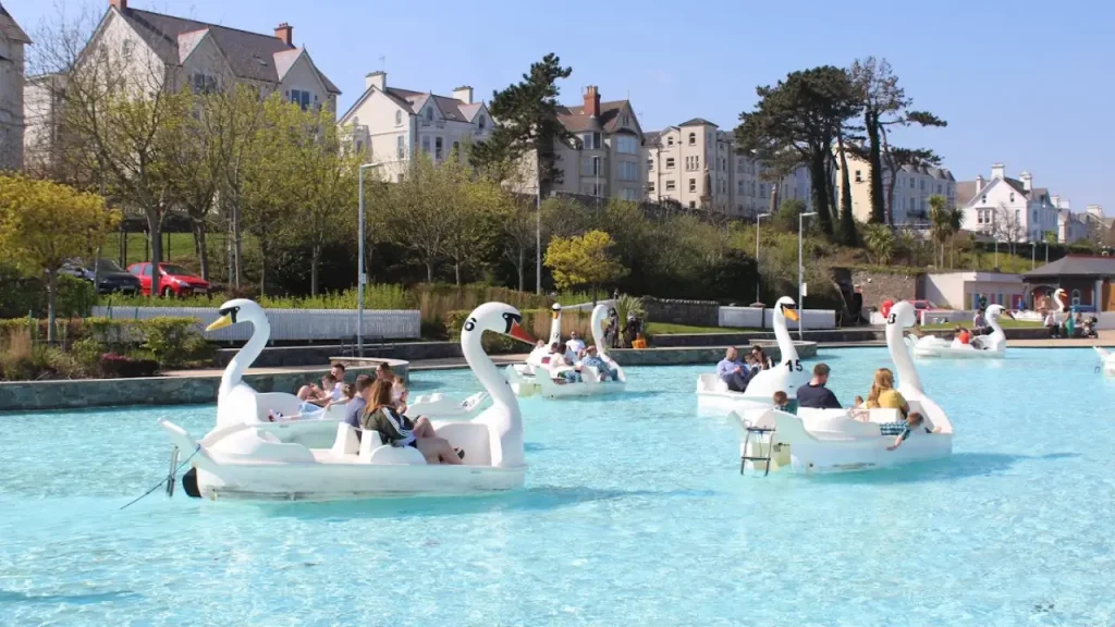Pickie Funpark swan pedal boats with families enjoying the water under a clear blue sky in Bangor, Northern Ireland.