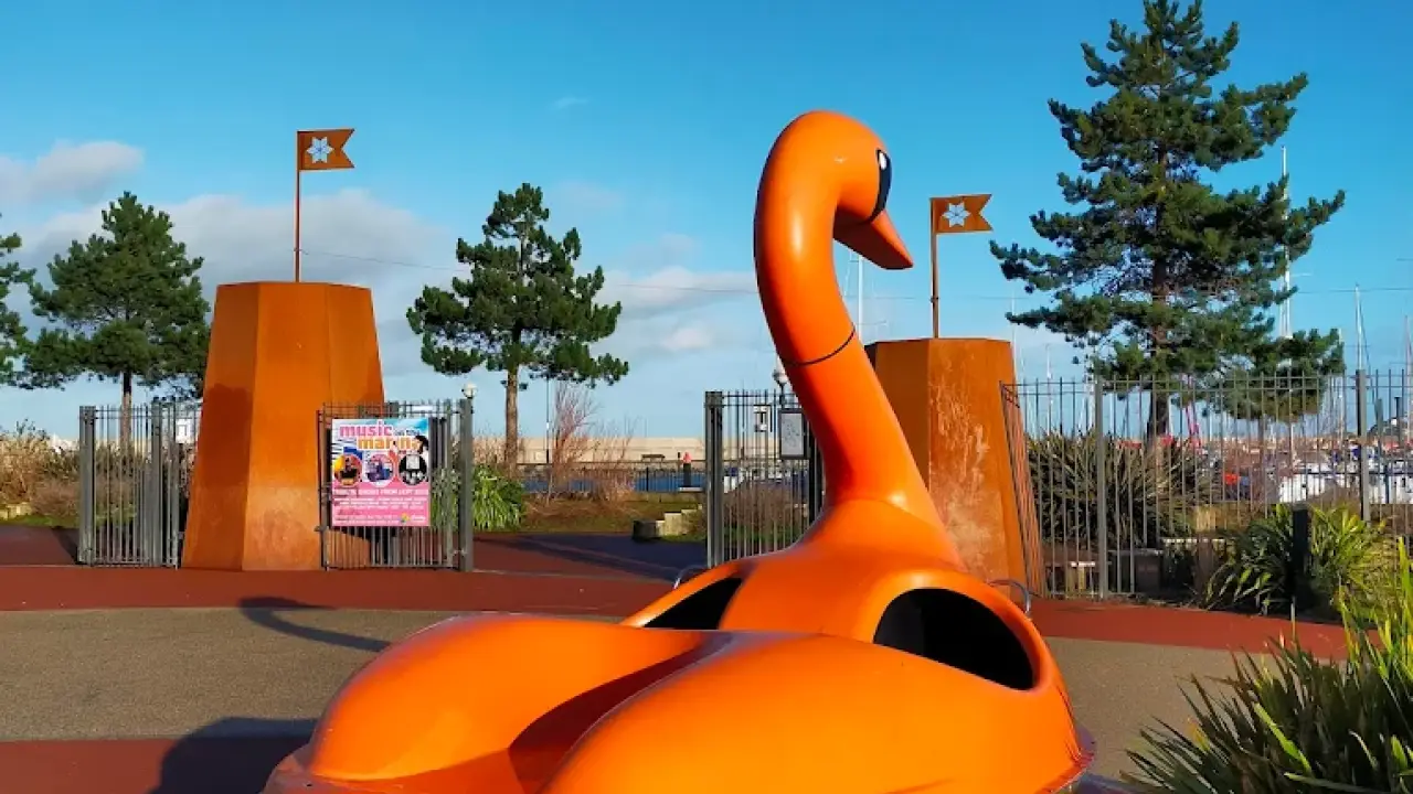 Orange swan boat displayed near the entrance of Pickie Funpark with trees and event banners in Bangor, Northern Ireland.