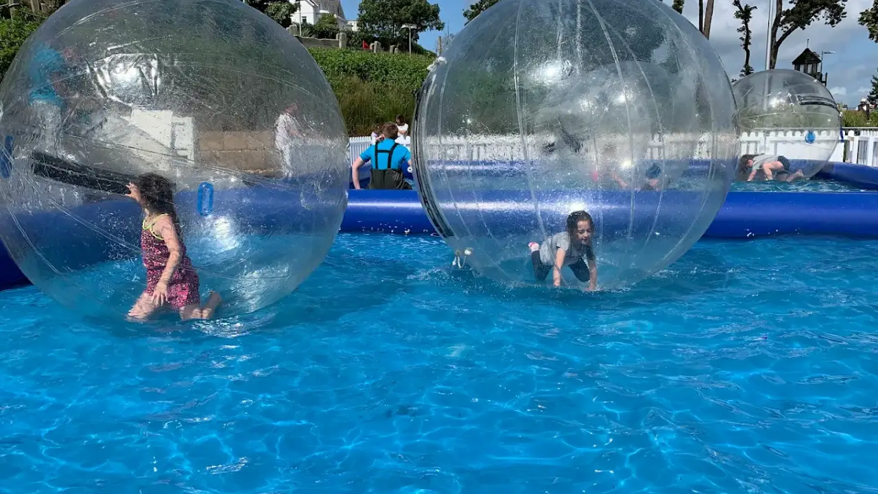 Children playing in inflatable water walking balls on a blue pool at Pickie Funpark water attraction in Bangor, Northern Ireland.