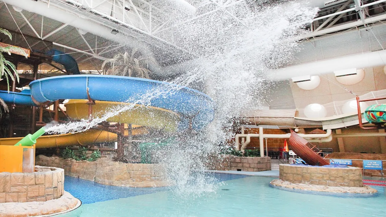Indoor water play area at Sandcastle Waterpark Blackpool with blue and yellow slides, palm trees, and a splash of water mid-air.