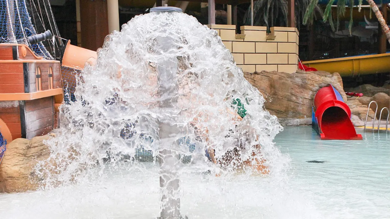 Children playing in a splash fountain beside a pirate ship-themed play zone and red toddler slide at Sandcastle Waterpark Blackpool.