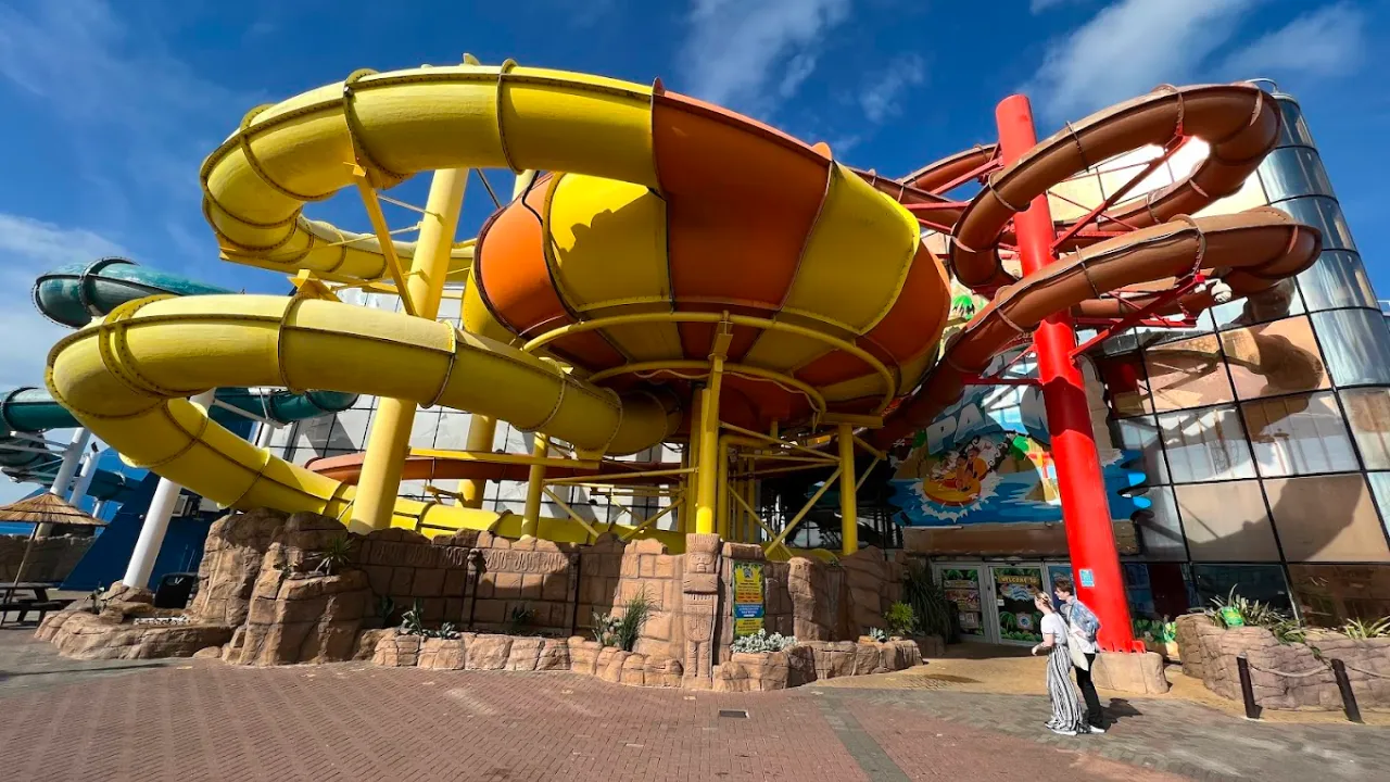 Bright yellow and orange spiral water slides wrapping around the exterior of Sandcastle Waterpark Blackpool under a sunny blue sky.