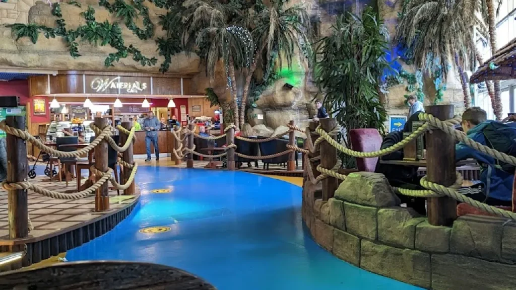 Guests dining at Waterfalls Café inside Sandcastle Waterpark Blackpool, surrounded by palm trees, tiki décor, and cosy seating.