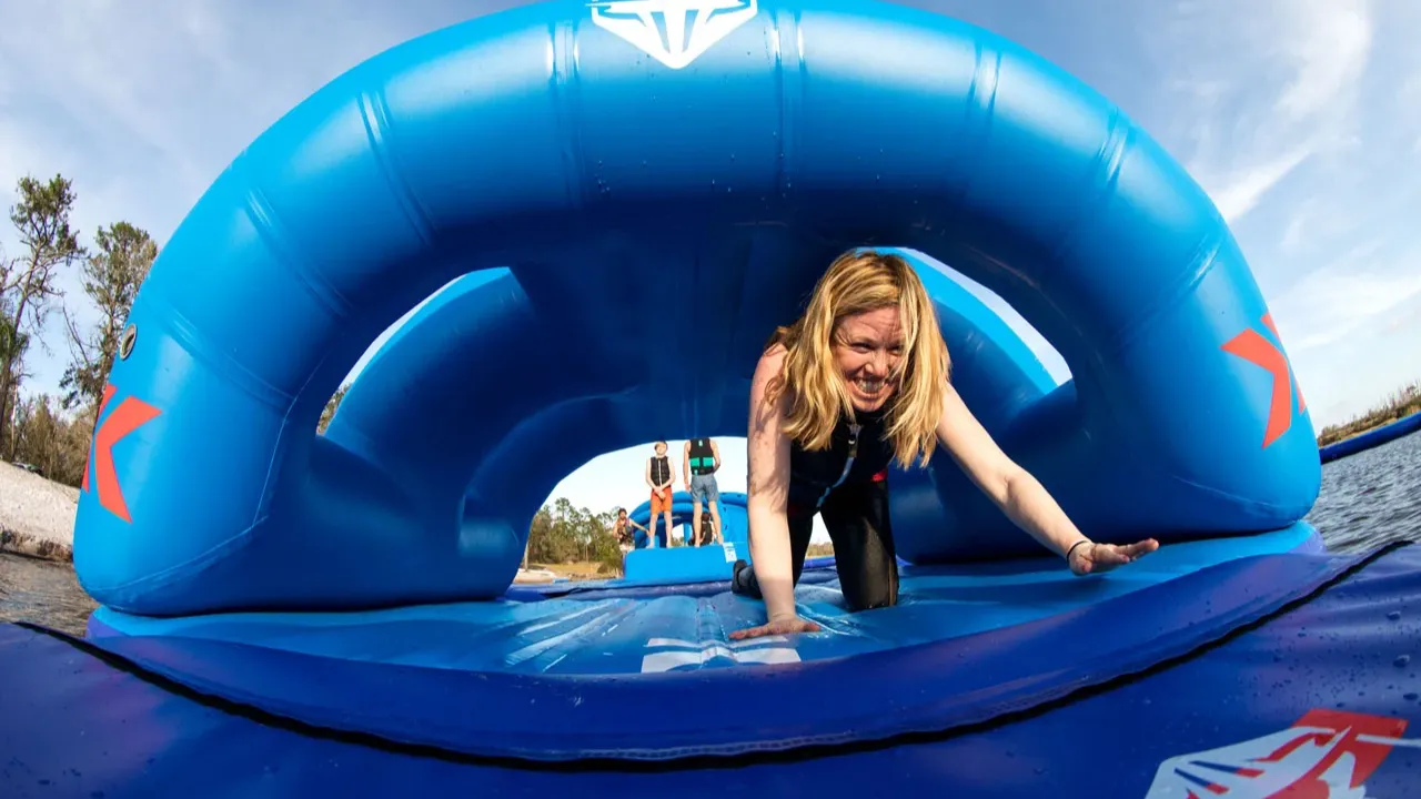 Woman smiling while crawling through a curved inflatable tunnel during a session at Sblash Aqua Park North Wales.