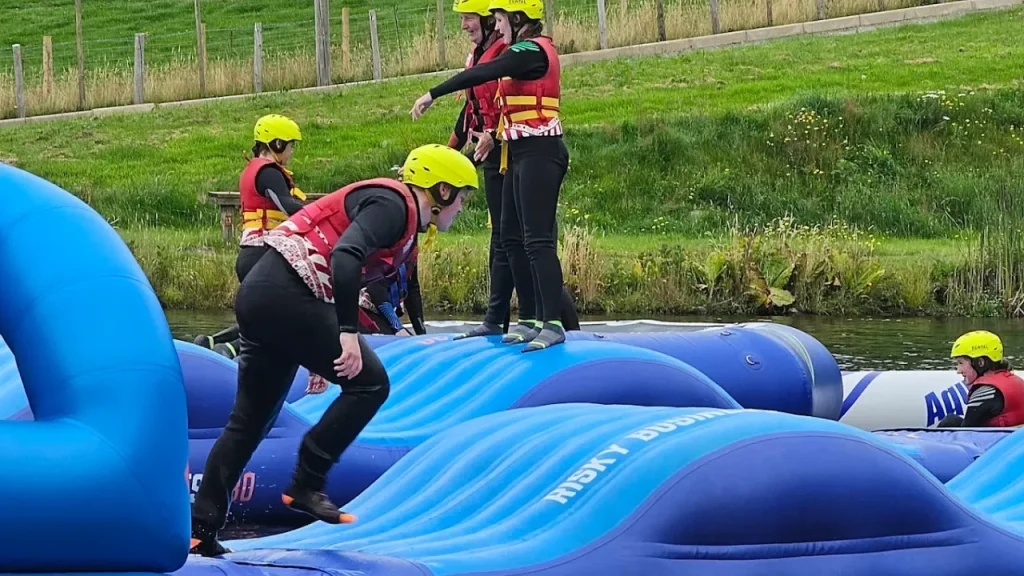 People navigating wave-shaped blue inflatables labelled “Risky Business” at Sblash Aqua Park Wales.