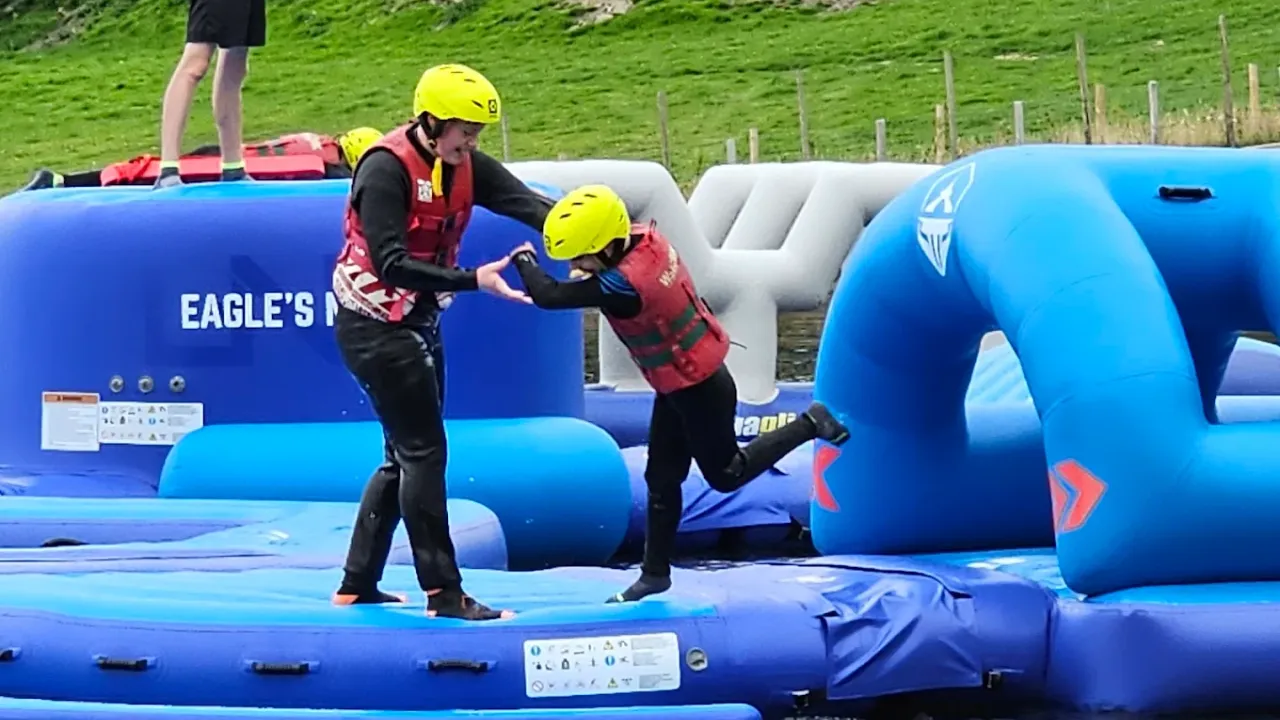 Parent assisting child on inflatable obstacle at Sblash Aqua Park, wearing safety helmets and life vests.