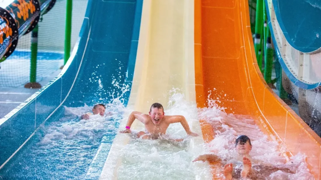 Close-up of children sliding down three brightly coloured water flumes at SC2 Rhyl, creating splashes as they reach the end of the slide.