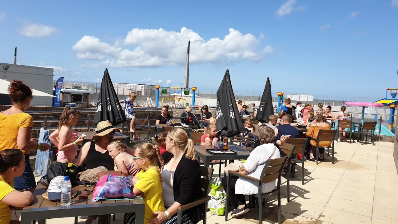 Crowds of families seated at the outdoor café terrace at SC2 Rhyl, overlooking the Splash Pad and enjoying the sunshine.