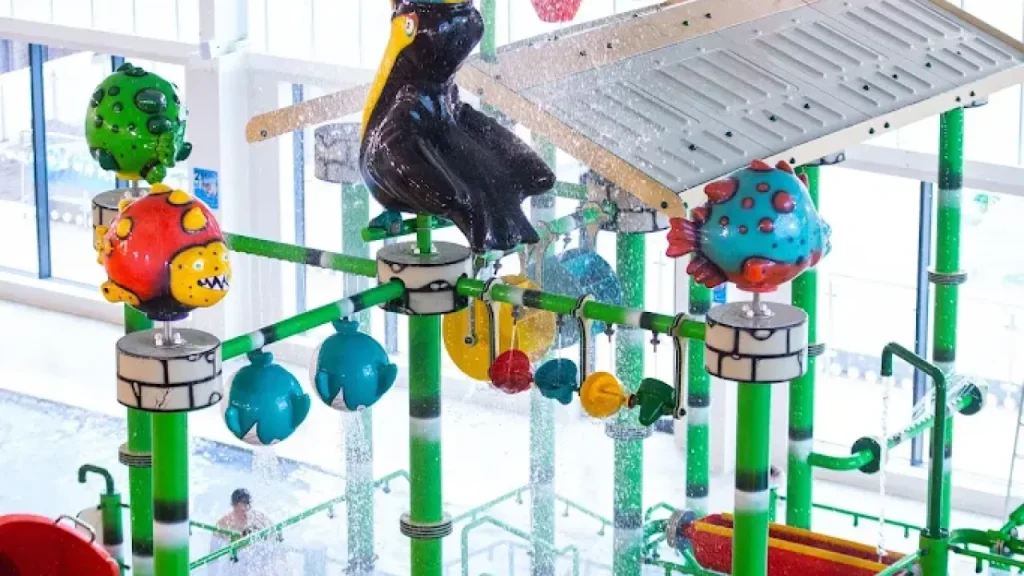 Detail view of SC2 Rhyl indoor water play zone showing colourful fish, penguin figures, and overhead sprinkler elements in a bright, child-friendly setup.