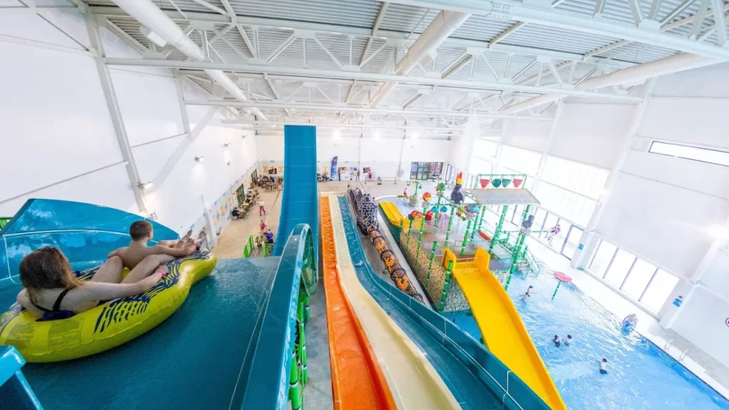 Riders at the top of the Boomerang slide inside SC2 Rhyl, overlooking multiple water slides, play structures, and a family-friendly swimming pool.