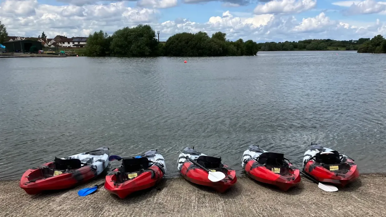 Row of red and grey kayaks lined up by the lakeside at South Lake Leisure Centre with calm water and cloudy sky in the background
