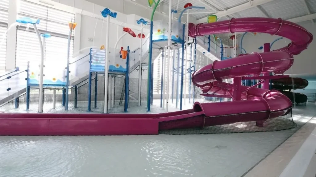 Indoor water play area at South Lake Leisure Centre with colourful splash features and bright pink spiral waterslide