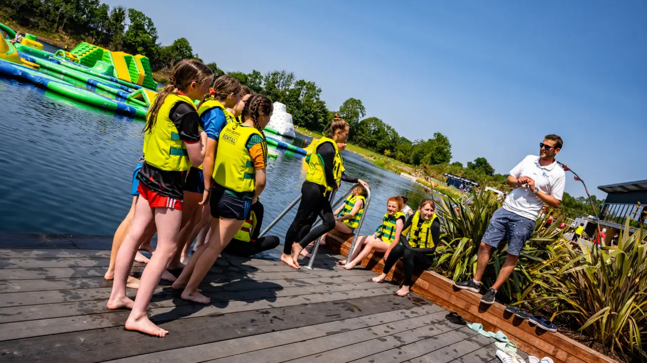 Children and instructor during a safety briefing at Splash Outdoor Waterpark in Northern Ireland, with AquaPark inflatables in the background.
