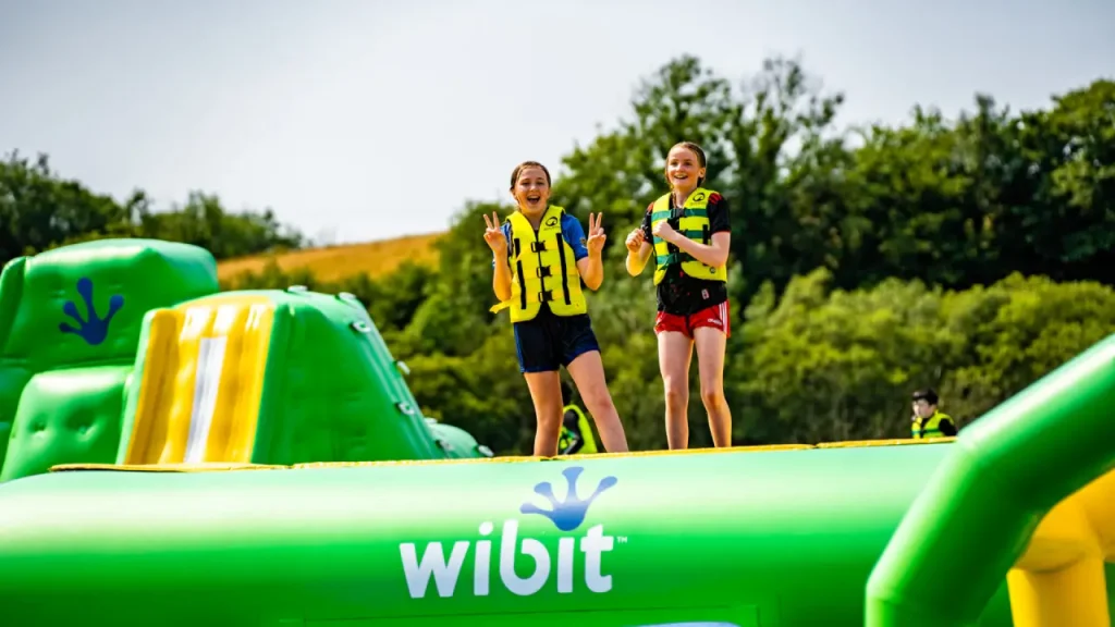 Two girls standing on the inflatable AquaPark at Splash Outdoor Waterpark in Northern Ireland, smiling and wearing yellow safety vests.