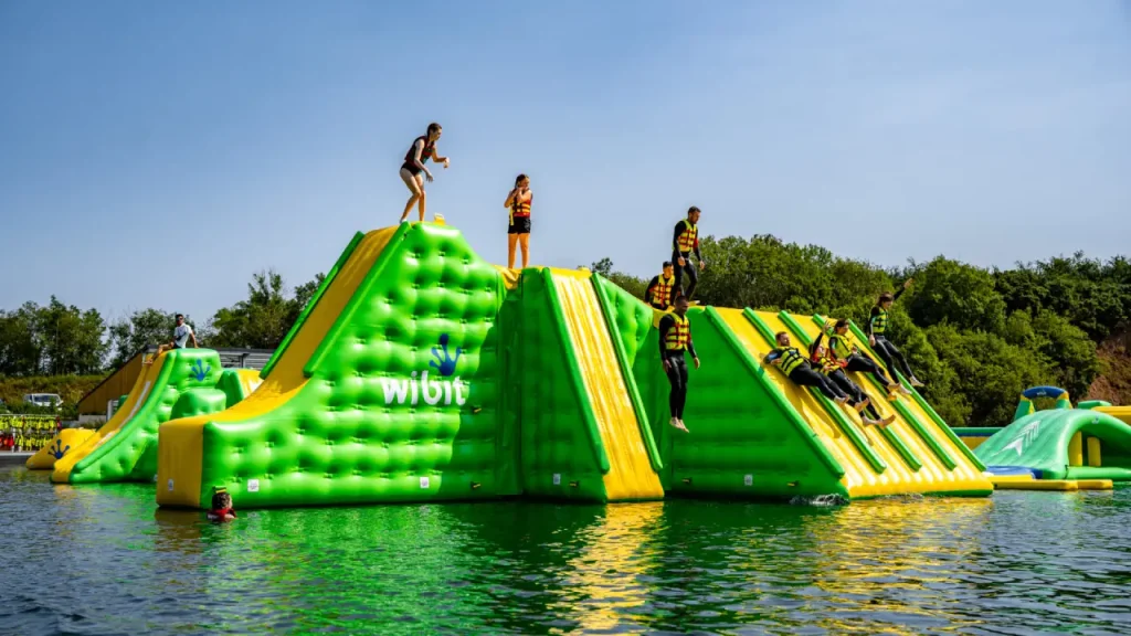 Group of people climbing and sliding on a large green and yellow inflatable structure at Splash Outdoor Waterpark AquaPark in Northern Ireland.