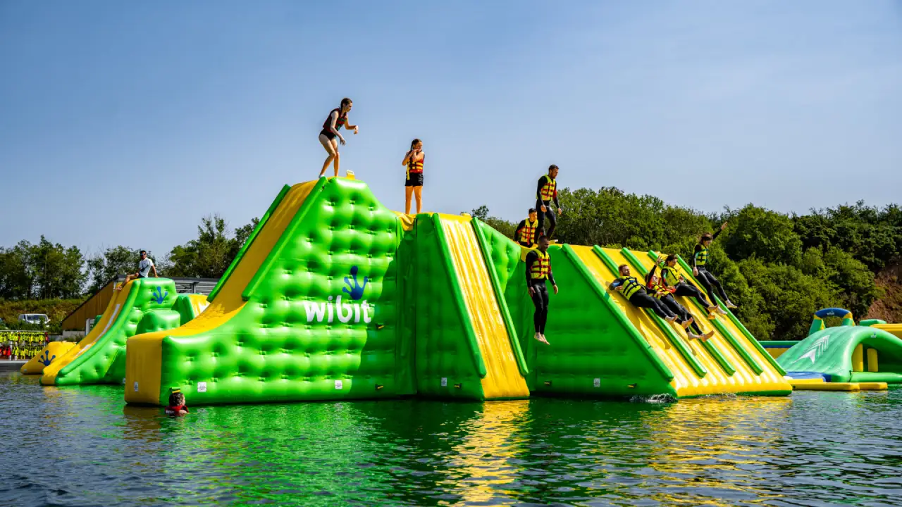 Group of people climbing and sliding on a large green and yellow inflatable structure at Splash Outdoor Waterpark AquaPark in Northern Ireland.