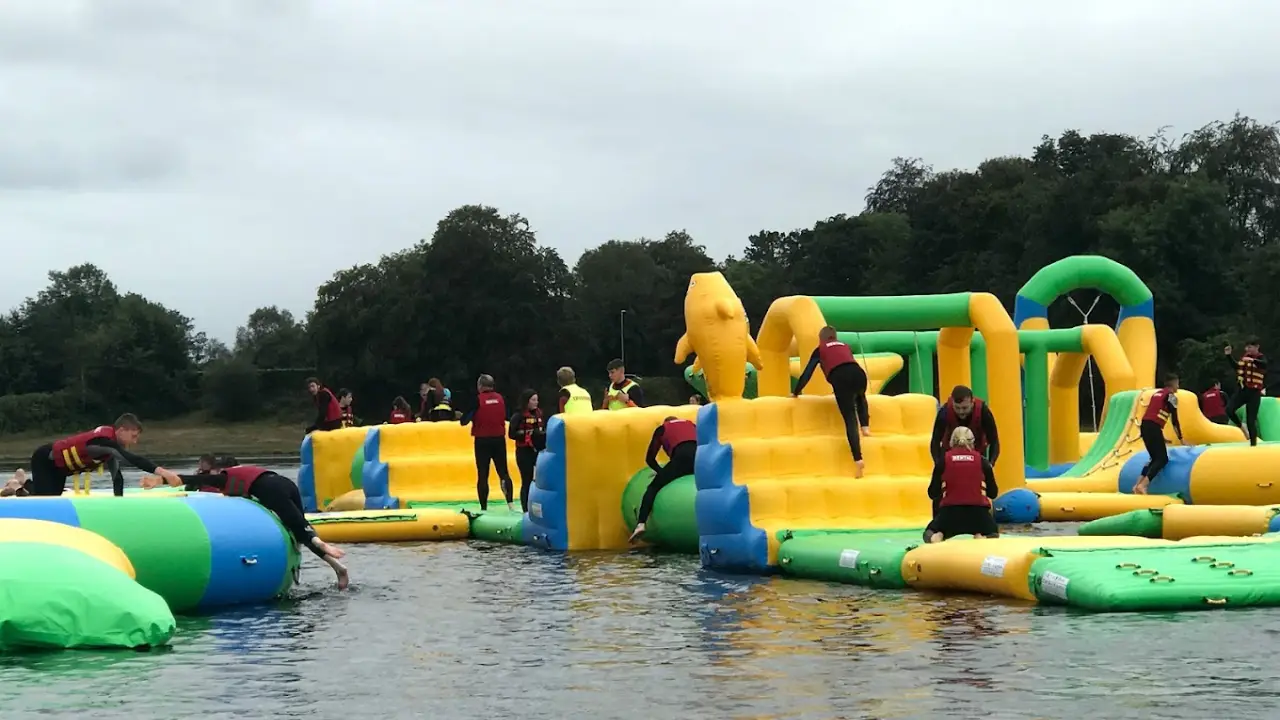 Visitors in life jackets climbing and sliding on colourful yellow and green inflatable obstacles at The Lake Kilrea Waterpark in Northern Ireland.