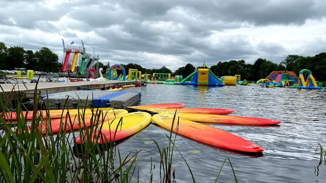 Bright red and yellow kayaks beside a dock with inflatable slides and obstacle courses in the background at The Lake Kilrea Waterpark, Northern Ireland.