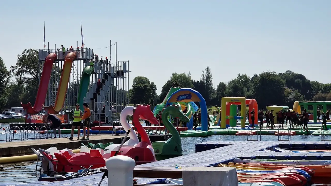 View of dragon-shaped paddle boats, tall red, yellow, and green slides, and inflatable obstacle courses at The Lake Kilrea Waterpark on a sunny day.