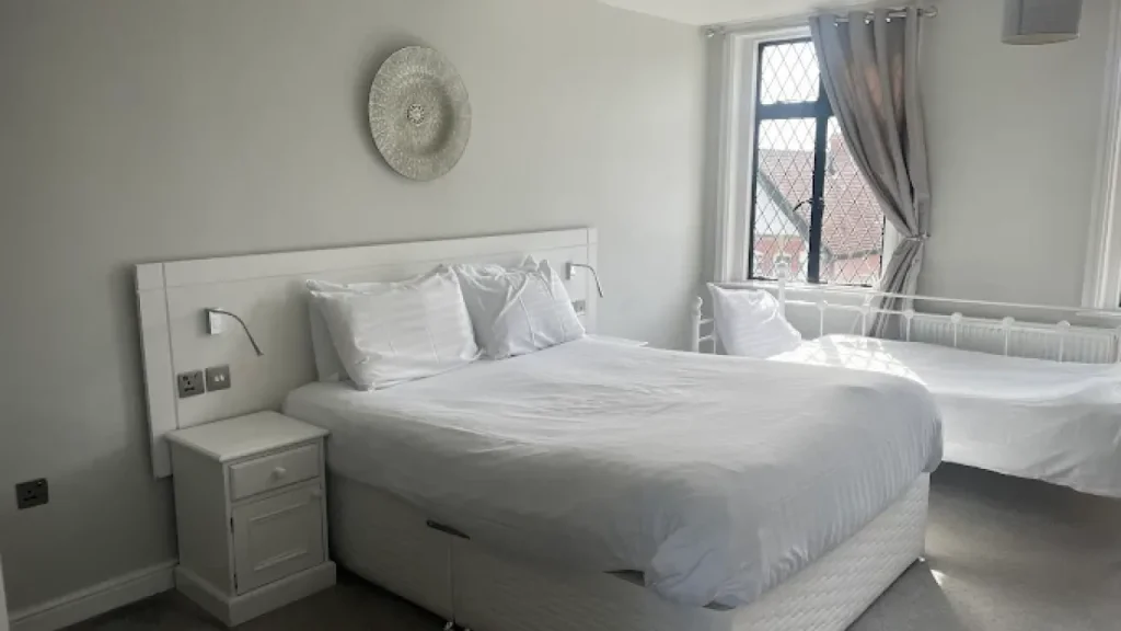 Spacious bedroom with white bedding, king-size bed, daybed, and leaded window at The White Hart Hotel near Alton Towers