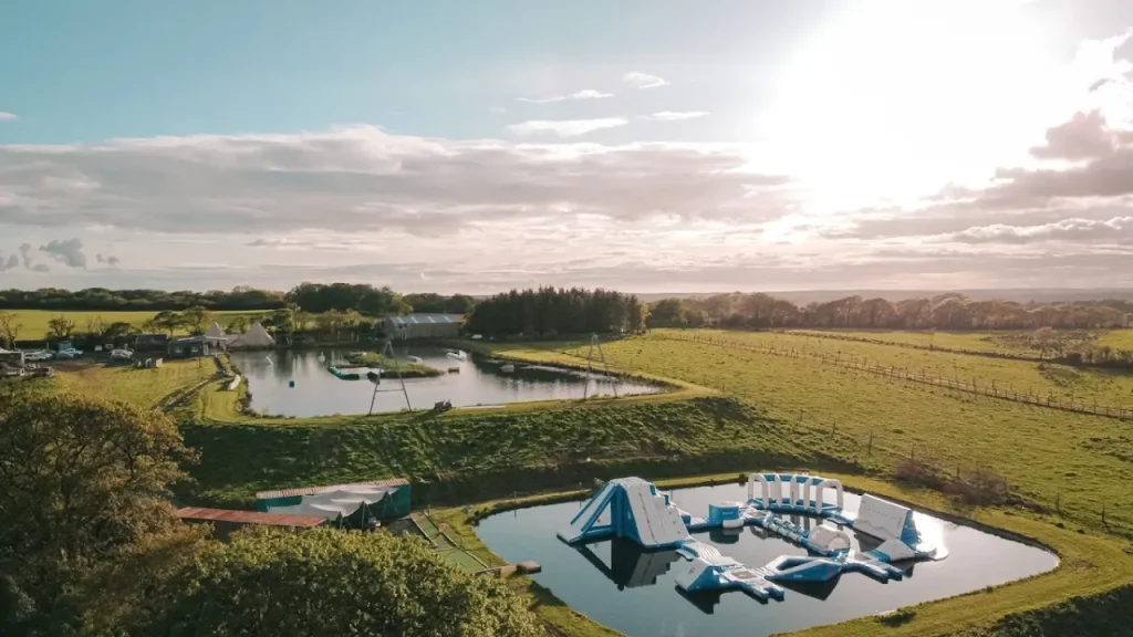 Aerial view of Wild Lakes Aqua Park in Wales featuring inflatable aqua course, surrounding lakes, green fields, and tipi tents in Narberth, Pembrokeshire.